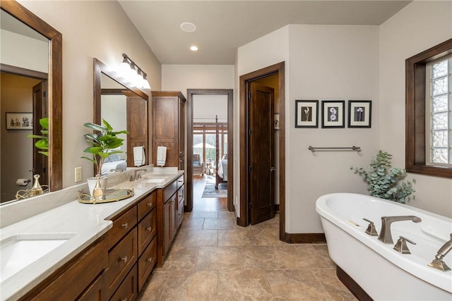 full bath featuring ensuite bath, a sink, a freestanding bath, double vanity, and baseboards