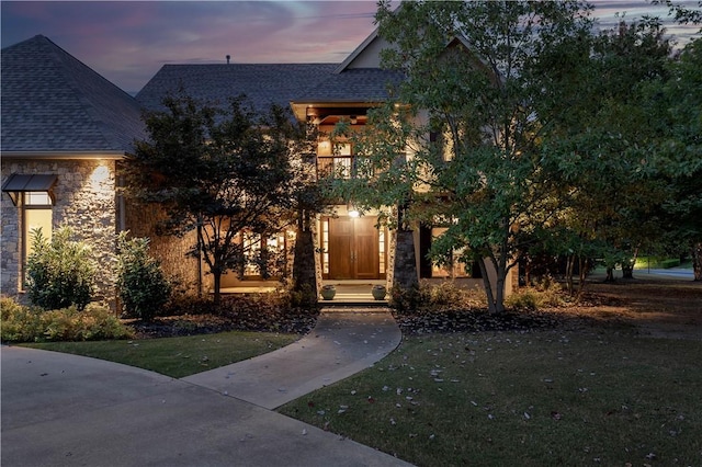 view of front of property featuring stone siding, roof with shingles, and a front yard