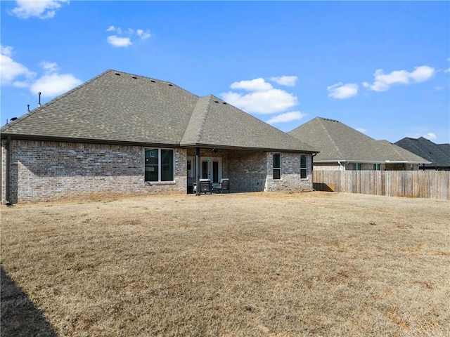 rear view of house featuring brick siding, fence, a lawn, and roof with shingles