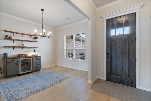 entrance foyer featuring baseboards, light wood-style flooring, wine cooler, crown molding, and a chandelier