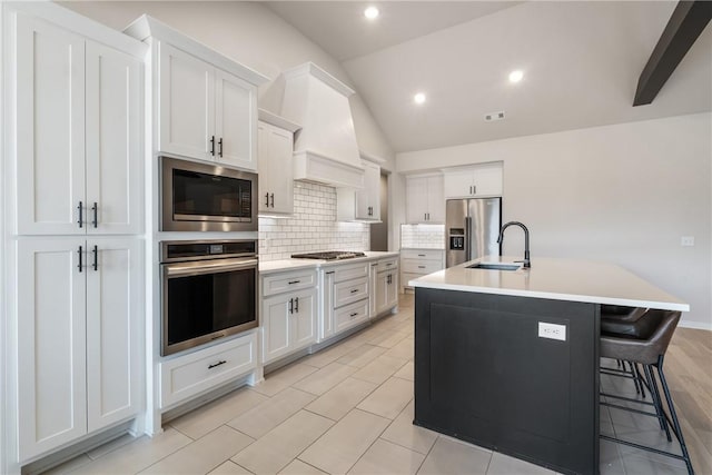 kitchen with appliances with stainless steel finishes, a sink, vaulted ceiling, light countertops, and backsplash