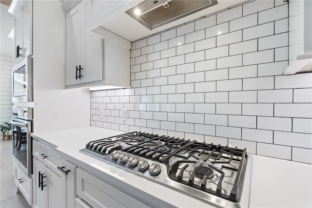 kitchen with stainless steel appliances, light countertops, decorative backsplash, white cabinetry, and under cabinet range hood