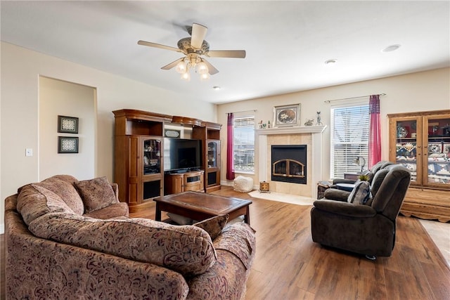 living area with a ceiling fan, a tile fireplace, and wood finished floors