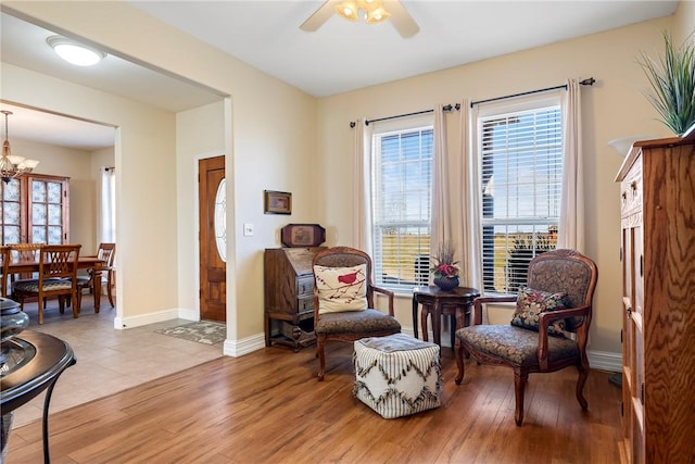 living area with ceiling fan with notable chandelier, light wood-style flooring, a wealth of natural light, and baseboards