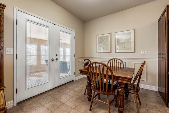 dining space featuring light tile patterned flooring, a decorative wall, and french doors