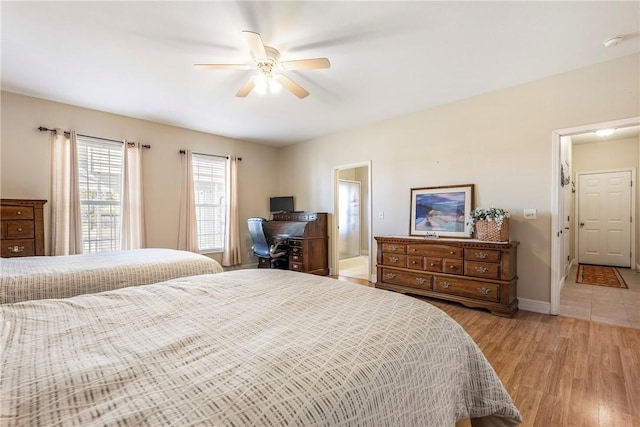 bedroom with ensuite bathroom, light wood finished floors, a ceiling fan, and baseboards