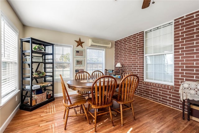 dining area with brick wall, an AC wall unit, wood finished floors, and baseboards