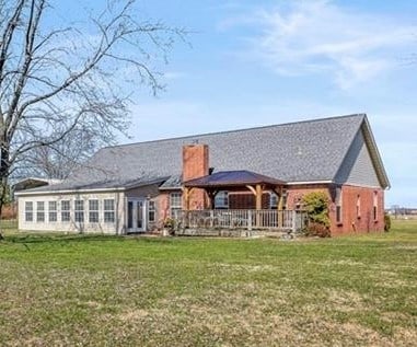 back of house with a chimney and a lawn