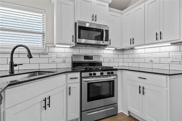 kitchen featuring tasteful backsplash, white cabinets, dark stone counters, stainless steel appliances, and a sink