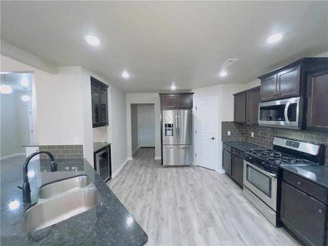 kitchen featuring dark brown cabinetry, light wood-style flooring, appliances with stainless steel finishes, a sink, and backsplash