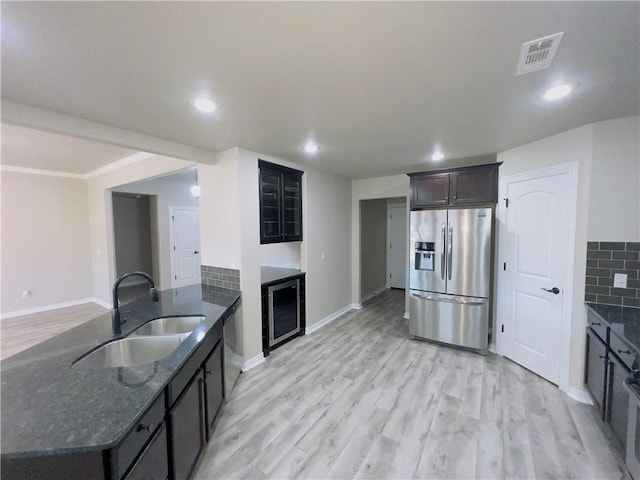 kitchen with stainless steel appliances, a sink, light wood-type flooring, backsplash, and dark stone counters