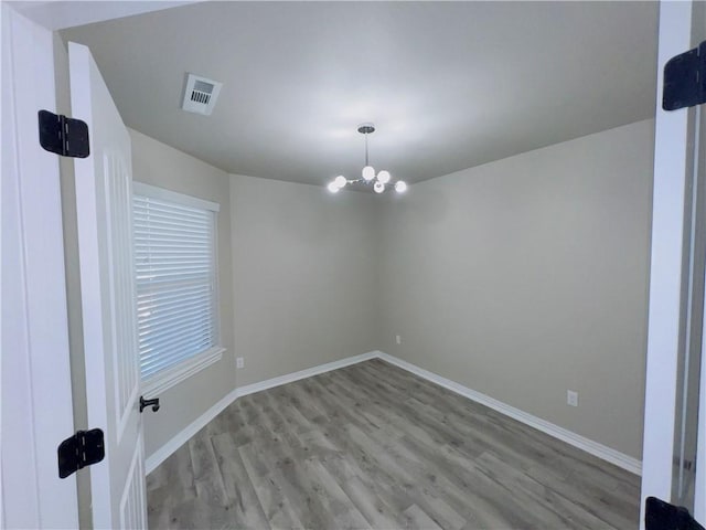 spare room with visible vents, a notable chandelier, baseboards, and wood finished floors