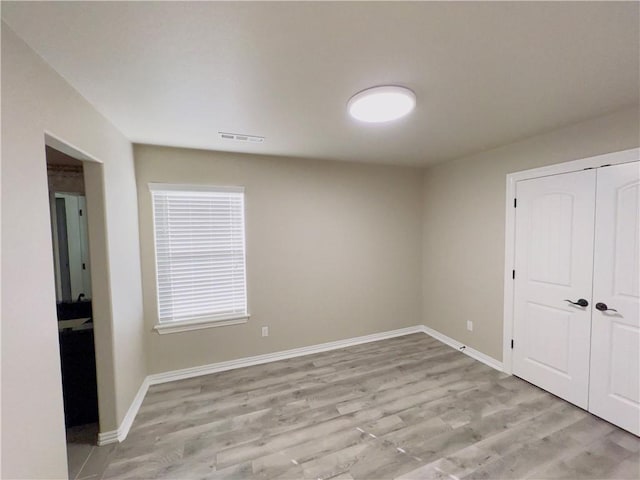 unfurnished bedroom featuring baseboards, a closet, visible vents, and light wood-style floors