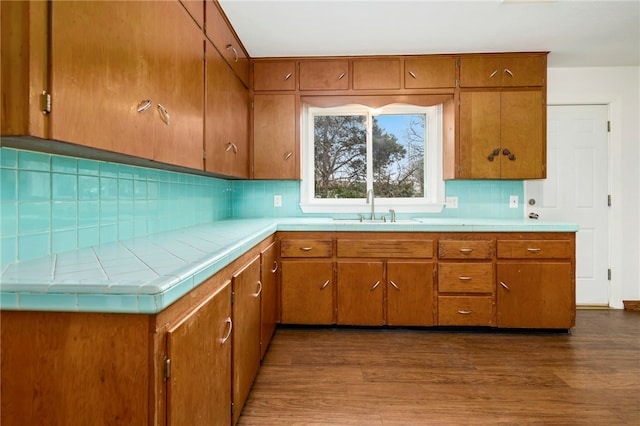 kitchen with backsplash, brown cabinetry, a sink, and wood finished floors