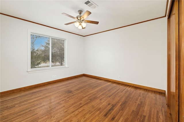 spare room with visible vents, ornamental molding, a ceiling fan, wood finished floors, and baseboards