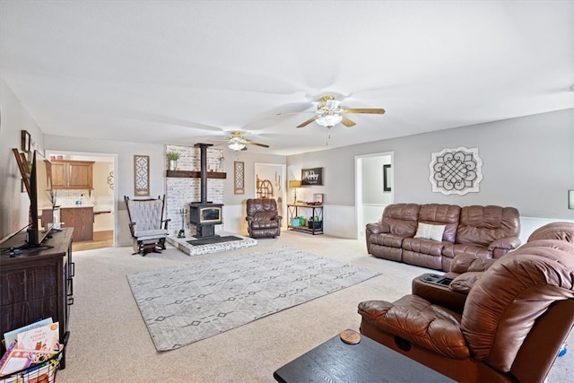 living room featuring ceiling fan, a wood stove, and light colored carpet