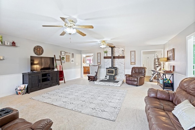 carpeted living room with a wood stove, ceiling fan, and wainscoting