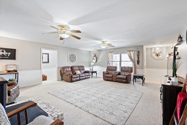 living area with a textured ceiling, carpet floors, ceiling fan, and wainscoting