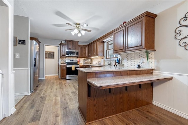 kitchen with backsplash, appliances with stainless steel finishes, a ceiling fan, light wood-type flooring, and a peninsula