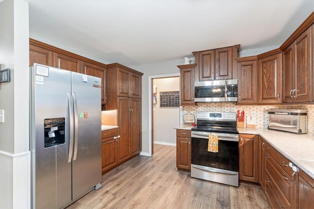 kitchen featuring appliances with stainless steel finishes, light wood-type flooring, brown cabinetry, and tasteful backsplash