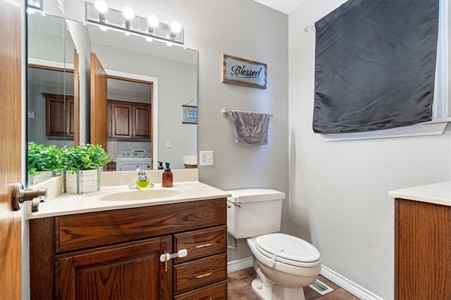 half bathroom with washer / clothes dryer, toilet, vanity, wood finished floors, and baseboards