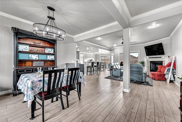 dining space with an inviting chandelier, light wood-style flooring, ornamental molding, and a glass covered fireplace