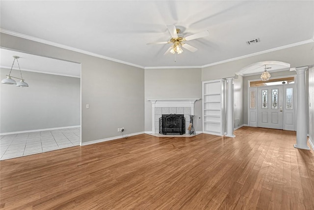 unfurnished living room featuring arched walkways, decorative columns, visible vents, a tiled fireplace, and wood finished floors