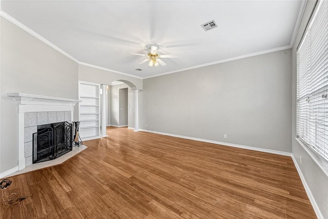 unfurnished living room featuring arched walkways, ceiling fan, a tile fireplace, wood finished floors, and visible vents