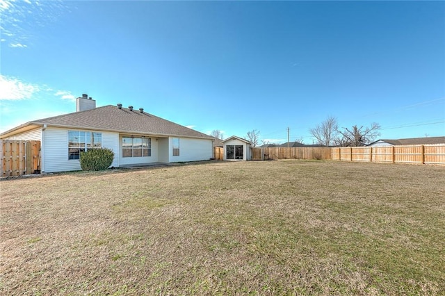 back of house featuring an outbuilding, a fenced backyard, a yard, a shed, and a chimney