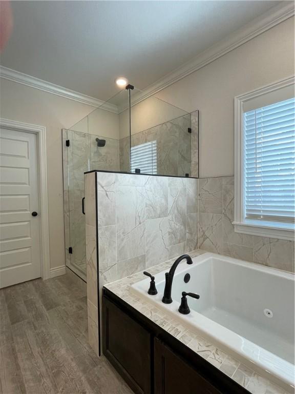 bathroom featuring a garden tub, a shower stall, crown molding, and wood finished floors