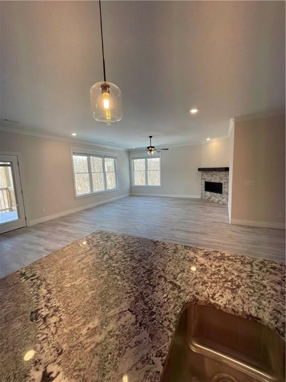 unfurnished living room featuring a fireplace, ornamental molding, light wood-style floors, ceiling fan, and baseboards