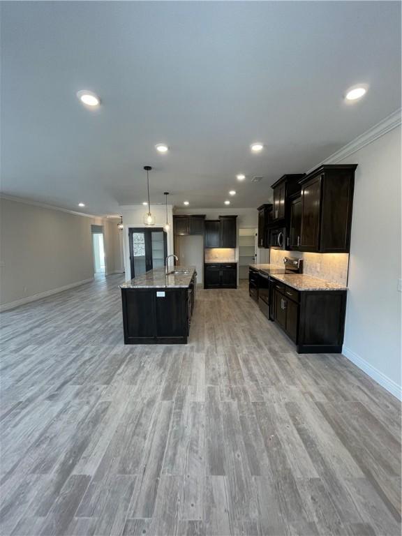 kitchen featuring ornamental molding, light wood-style floors, open floor plan, a sink, and baseboards