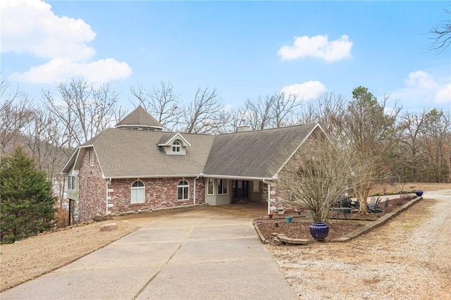 view of front of house featuring roof with shingles, a chimney, concrete driveway, and brick siding