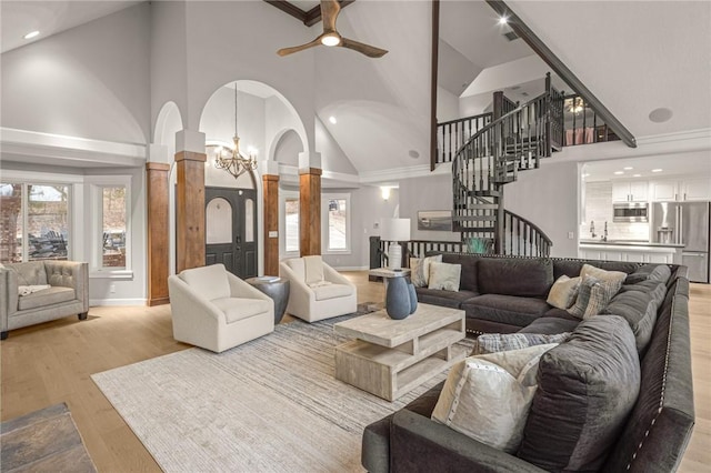 living room featuring arched walkways, stairs, high vaulted ceiling, ceiling fan with notable chandelier, and ornate columns