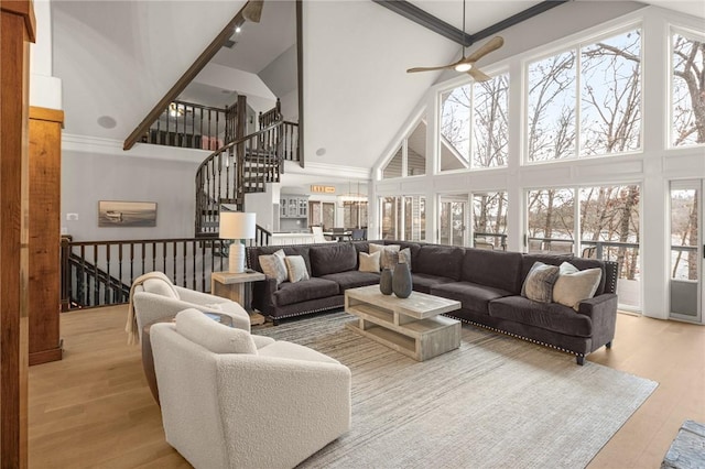 living area with a towering ceiling, ceiling fan, stairs, and wood finished floors