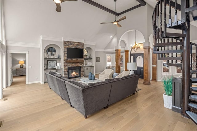 living room featuring arched walkways, stairs, crown molding, a stone fireplace, and ceiling fan with notable chandelier