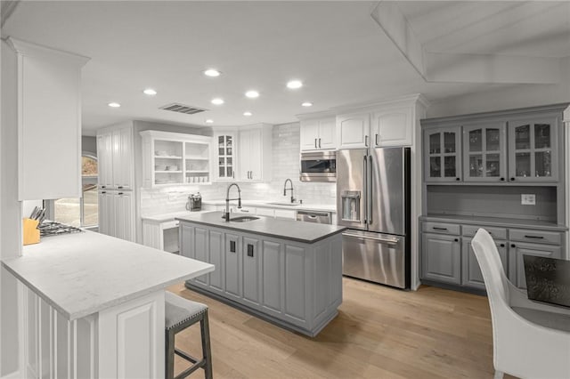 kitchen with gray cabinetry, visible vents, light wood-style floors, appliances with stainless steel finishes, and glass insert cabinets