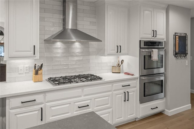 kitchen featuring stainless steel appliances, wall chimney range hood, light wood-type flooring, and white cabinetry