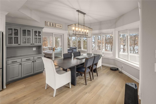 dining area with baseboards, a notable chandelier, and light wood finished floors