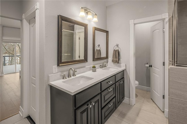 full bathroom with toilet, double vanity, baseboards, and a sink