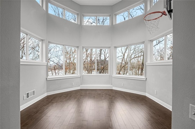unfurnished sunroom featuring plenty of natural light, baseboards, visible vents, and hardwood / wood-style flooring