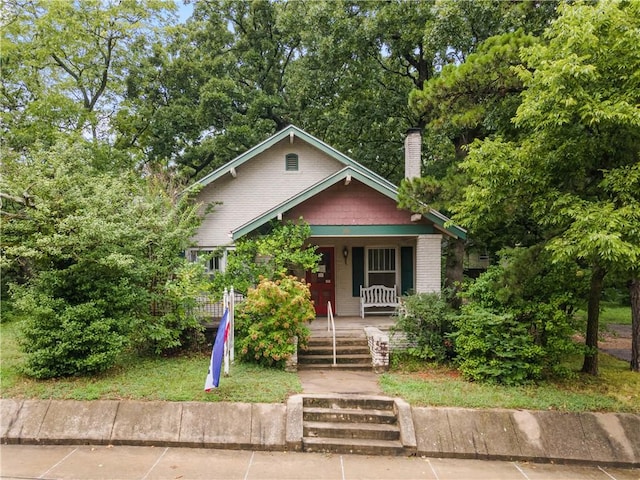 bungalow-style home featuring covered porch, brick siding, and a chimney