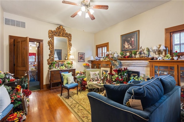 living area featuring a brick fireplace, visible vents, ceiling fan, and hardwood / wood-style floors