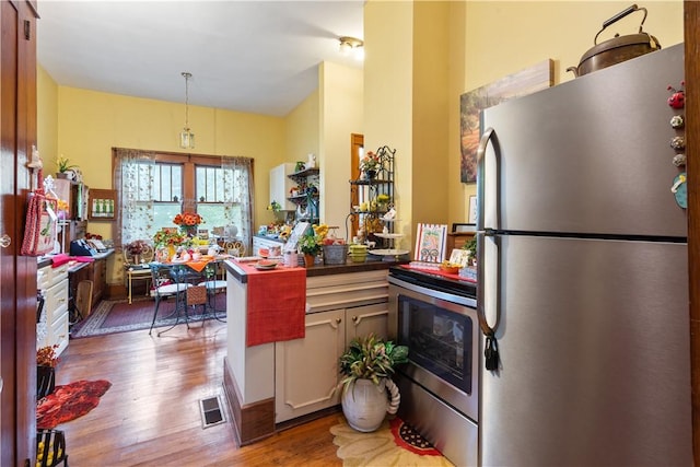 kitchen featuring stainless steel appliances, a peninsula, wood finished floors, visible vents, and dark countertops