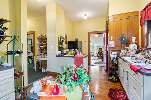 kitchen with a sink, wood finished floors, white cabinets, freestanding refrigerator, and dark countertops