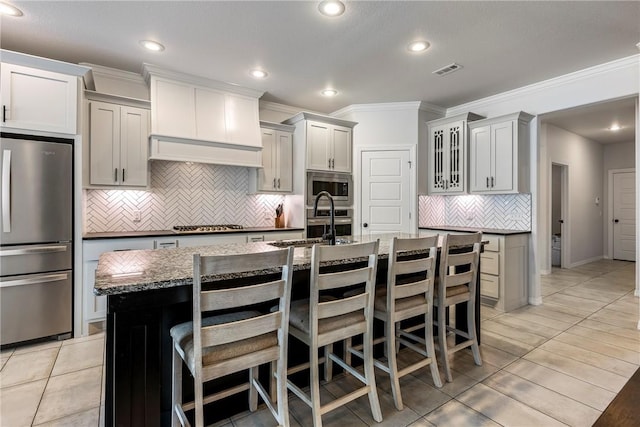 kitchen with stainless steel appliances, visible vents, an island with sink, and a kitchen bar