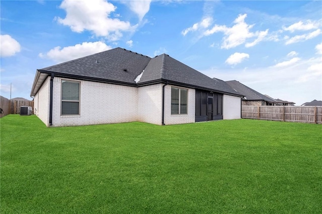 back of property featuring roof with shingles, a fenced backyard, a lawn, and brick siding