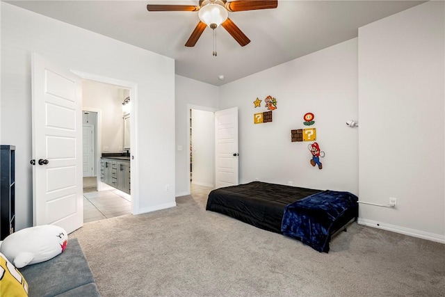 bedroom with baseboards, ensuite bath, a ceiling fan, and light colored carpet