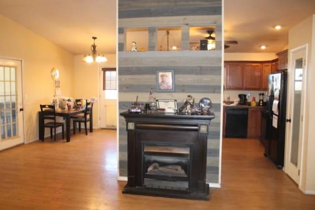 kitchen featuring brown cabinetry, a glass covered fireplace, lofted ceiling, wood finished floors, and black appliances