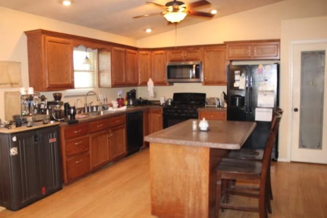 kitchen with light wood-type flooring, vaulted ceiling, black appliances, and a breakfast bar area